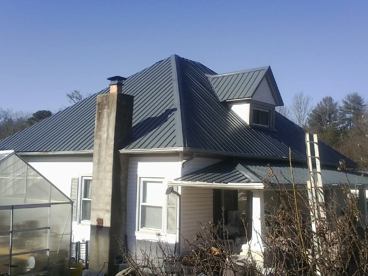 Dark blue standing seam metal roof on a white farmhouse with dormer — Slate & Tile Roof Repair by Roofing Brothers in Millbrook