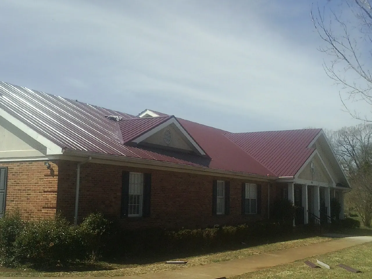 Red metal roof with gabled entries on a long brick building, from a Hail Damage Roof Repair job in Millbrook