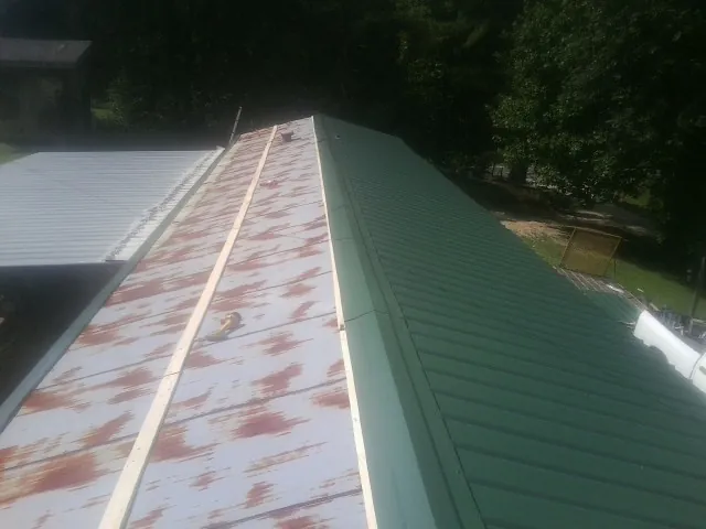 Old rusted panels beside newly installed green metal roofing — Wind Damage Roof Repair by Roofing Brothers in Millbrook