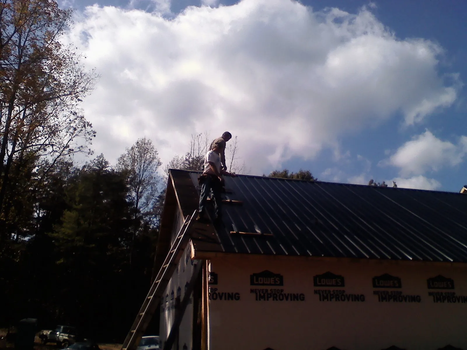Roofer fastening dark metal panels high against a cloudy sky, from a Roof Inspection job in Millbrook