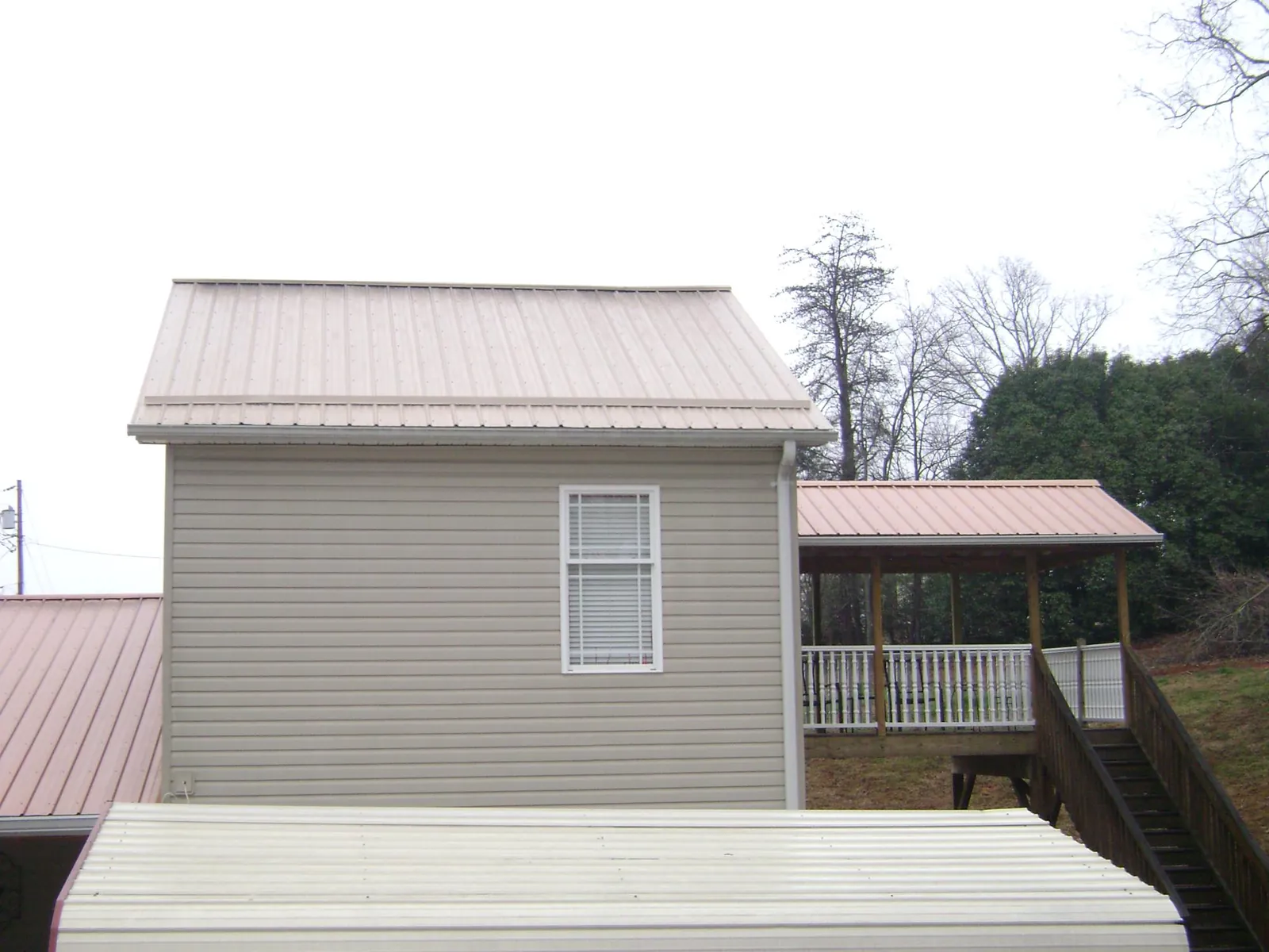 Tan metal roofs on a two story addition and attached porch, from a Roof Replacement job in Millbrook